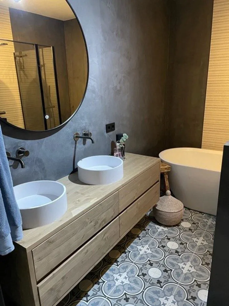 Betonlook badkamer met donkere wanden, dubbele waskom en patroontegels op de vloer