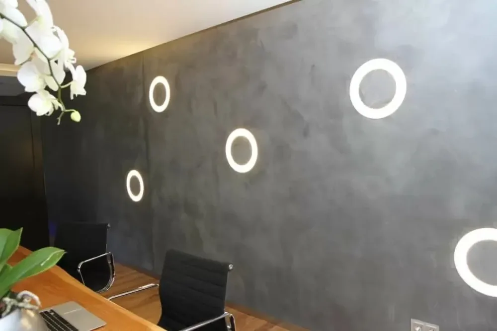 Antraciet beton ciré wand met ronde ledverlichting in een werkruimte