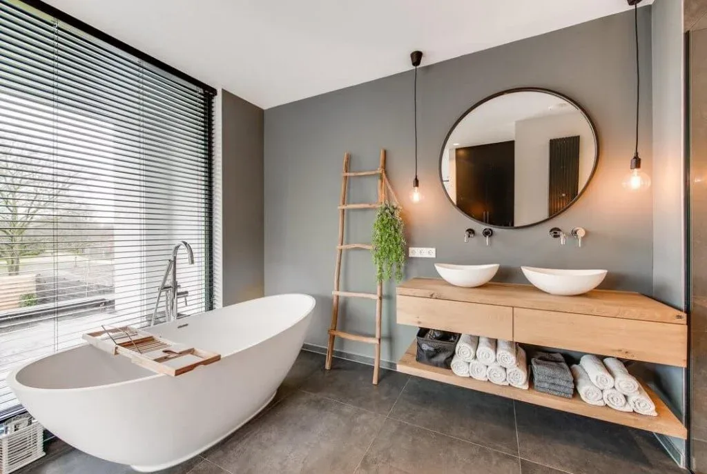 Badkamer met grijze wanden, vrijstaand bad en dubbele waskommen op een houten meubel